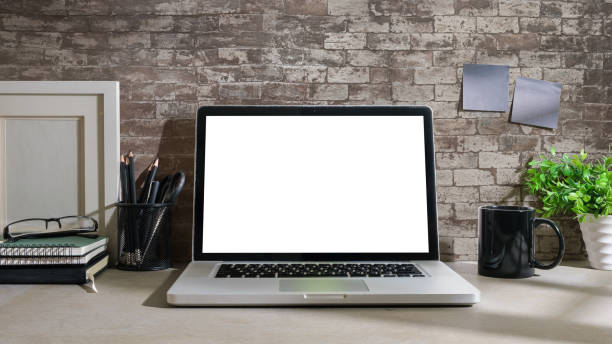 istock Mockup computer laptop, coffee cup, books and pencil holder on white table with brick wall. 1690019579