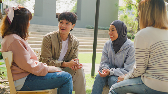 Small Asian group of people sit in a close circle and talk to a therapist in park. Smile people sharing story happy speak diverse people sitting in circle at group therapy session with psychologist.