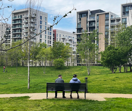 People sitting on a bench in a park, by apartments in a residential area in Stratford, east London