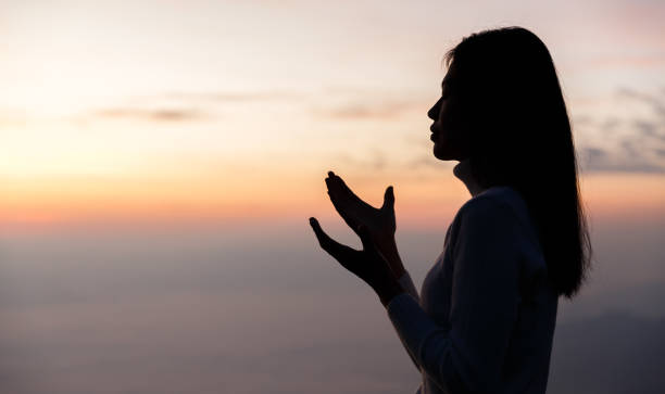 silhouette of woman praying for thank god praying with her hands together to think of a loving god, we praise god with light flare in the green nature. - god freedom arms raised high angle view imagens e fotografias de stock