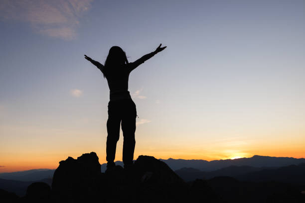 silhouette einer frau auf dem gipfel des berges, die auf die sonne, die freiheit blickt, betet auf dem gipfel des berges. - god freedom arms raised high angle view stock-fotos und bilder