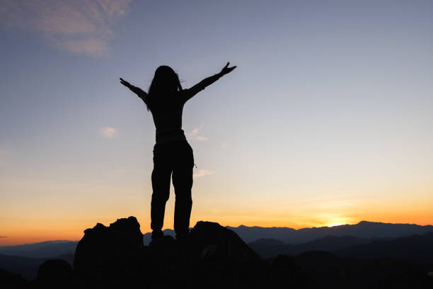 山の頂上に太陽を見つめ、自由、山の頂上で祈る女性のシルエット。 - god freedom arms raised high angle view ス��トックフォトと画像