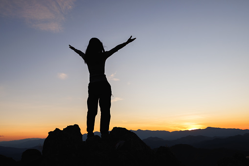 Silhouette of woman on top of the mountain looking to the sun, freedom, pray on top of mountain.
