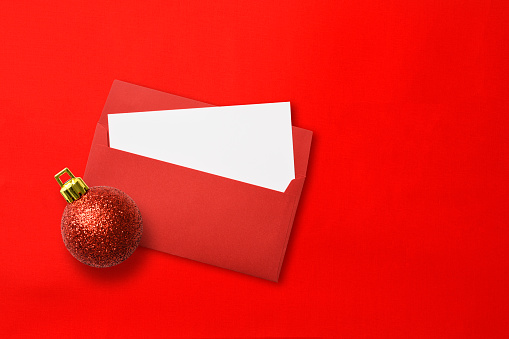 Overhead shot of red envelope and blank card with Christmas ball, on red background with copy space.