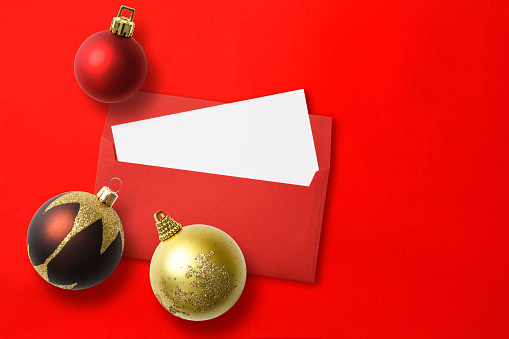 Overhead shot of red envelope and blank card with Christmas balls, on red background with copy space.