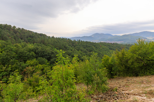 Composition of the Balkan mountains and the green forest near them , during early autumn time.