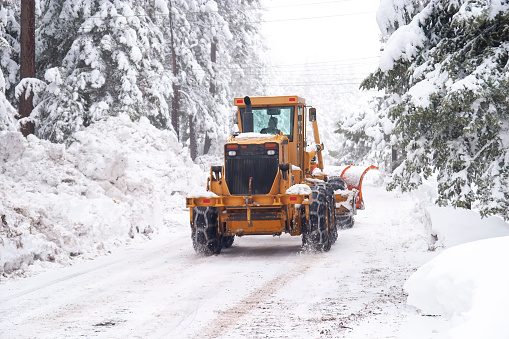 Snow plow tractor working in blizzard conditions on a road