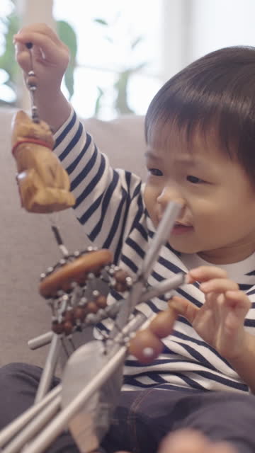 Adorable Asian baby boy playing wind chime on couch at home curiously.