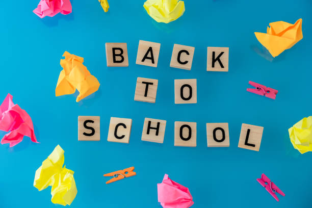 pädagogische begrüßungsankündigung für schüler und lehrer. spruch zurück zur schule-text auf holzklötzen auf buntem blauem hintergrund rund um schreibwarenbedarf. draufsicht flat lay konzept levitation des neuen schuljahres - fall semester stock-fotos und bilder