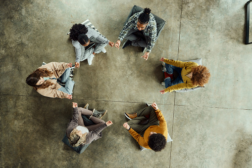 High angle view of team of creative people exercising Yoga in Lotus position on floor in the office. Copy space.