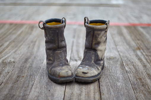 Old, brown leather safety shoes with worn out steel toe on wooden deck.