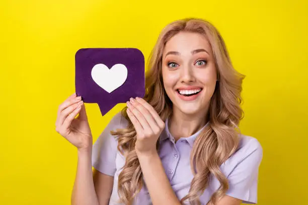 Photo of Photo of positive excited woman dressed violet t-shirt rising heart like feedback card isolated yellow color background