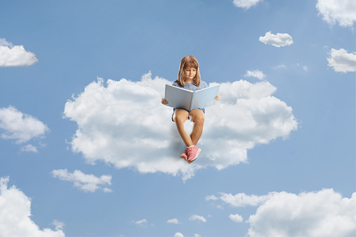 Little girl sitting on a cloud and reading a book up in the sky