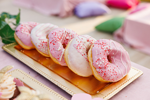 Doughnuts with pink and white sugar paste glaze and red sprinkles lined up on display tray at confectioner's