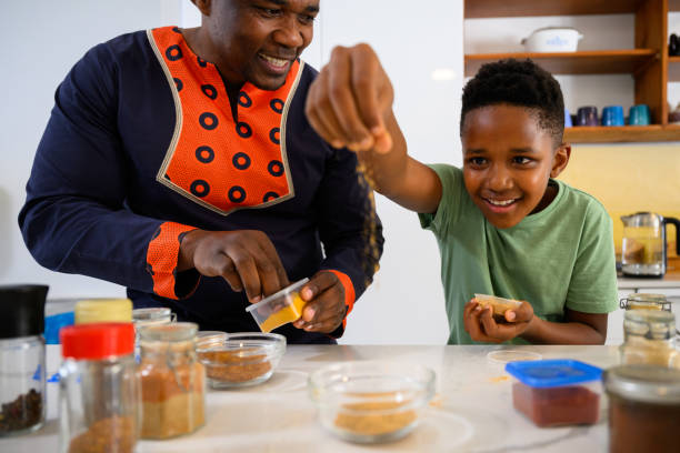 istock Excited boy sprinkling spices into mixing bowl while father watches 1690264108