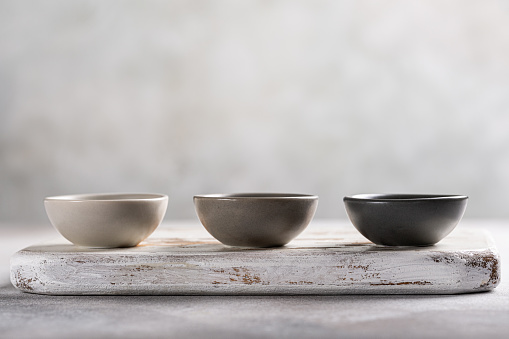 Three empty gray small bowls on old white wooden board. Mini plates for sauce or dip. Copy space