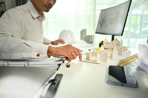 Cropped shot of architect man examining building model, working on project of residential at desk.