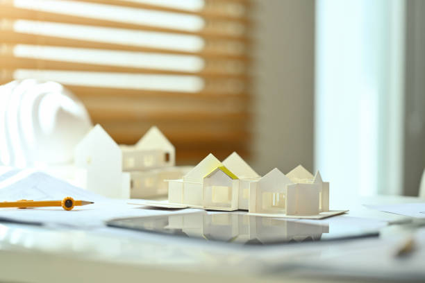 istock Architectural model of houses on desk with drawing tools and blueprints. Building, construction and architect concept. 1690286472