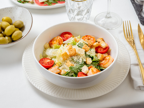 Caesar salad with shrimps on plate in restaurant table interior. Classic caesar shrimp salad closeup view