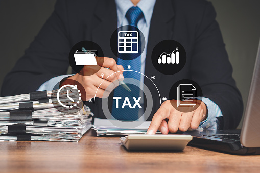 Tax day concept. A businessman uses a calculator to calculate taxes while sitting in the office. Assistance with filing tax forms and calculations. Business icons on a virtual screen