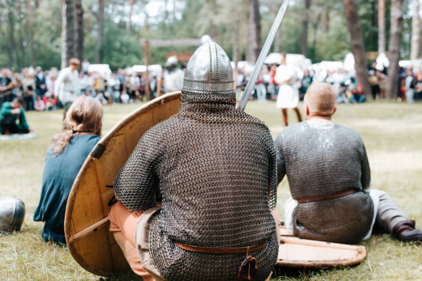 istock Resting warrior barbarian in armor, helmet and with a sword outdoors, back view. Medieval festival reconstruction 1690316882