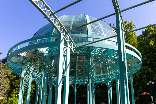 Green glass pavilion with a dome above mineral water hot spring in Borjomi Central Park, spa resort town in Georgia, Caucasus Mountains.
