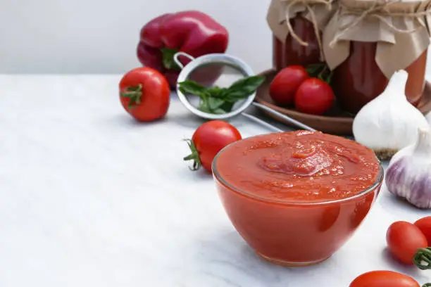 Tomato sauce in a glass bowl. Red tomatoes, sweet pepper, garlic and basil on background. Side view, space for text.