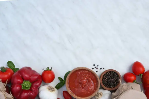 Wooden bowl of tomato sauce with fresh ingredients on white marble background. Top view. Space for text