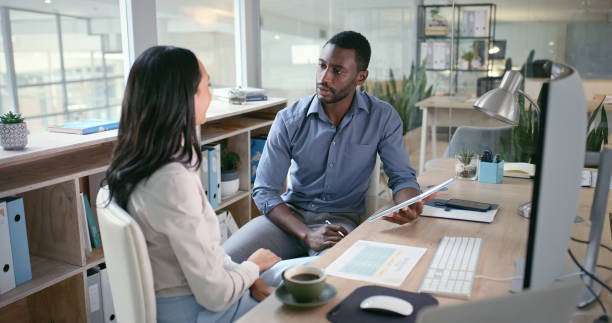 istock Paperwork, teamwork or business people talking in training, coaching or mentorship in office. Research, collaboration or black man speaking of web design or documents data on tablet to woman at night 1690348524