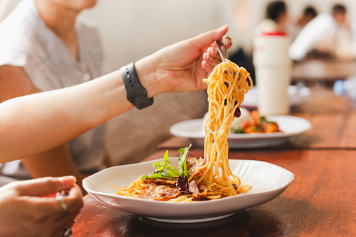 Woman eating spaghetti with friend in restaurant