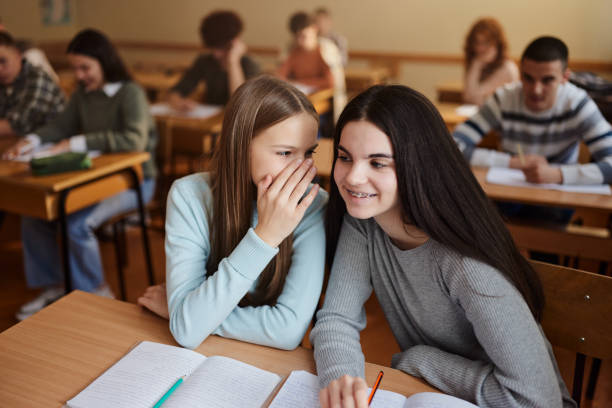 Happy female students whispering on a class at high school.