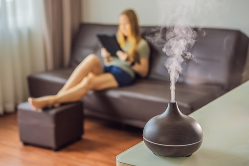 Aromatherapy Concept. Wooden Electric Ultrasonic Essential Oil Aroma Diffuser and Humidifier. Ultrasonic aroma diffuser for home. Woman resting at home.