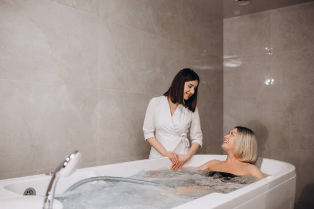 jeune femme pendant l’hydromassage dans un salon de beauté. concept de soins du corps et spa. la masseuse masse la fille dans le bain avec un jet d’eau. photo de haute qualité - hidromassage inside of wet luxury photos et images de collection