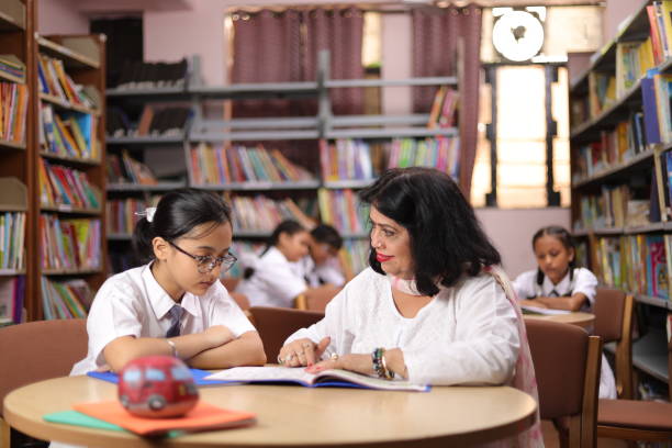 istock Confident school teacher teaching, educating  girl child student in library, extra classes, education, reading book, smart. 1690386049