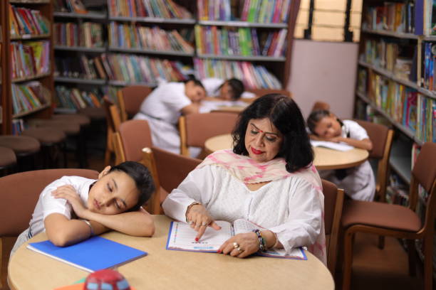 istock School teacher teaching, educating  girl child student in library, students sleeping, head down, boring. 1690390903