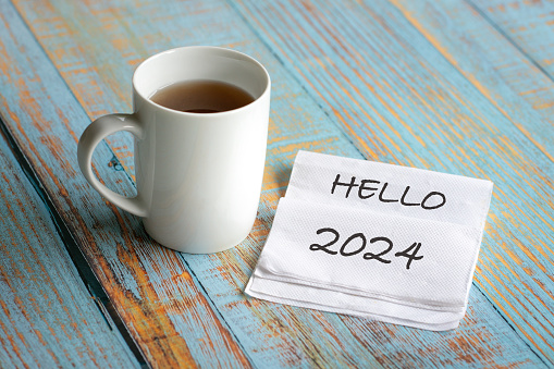 Hello 2024 on piece of tissue next to a white cup of coffee.