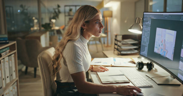 Business woman, night and graphic designer on computer in office at table working on deadline. Creative, serious and professional at desk, editing photo on software and focus on retouching in startup