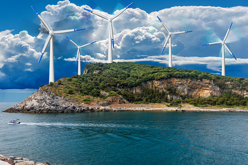 Group of white and blue wind turbines above an island in the sea against a storm clouds. Photography. Renewable energy concept.