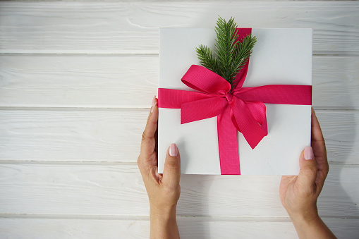 Women's hands hold a Christmas gift with a pink bow and a sprig of pine needles