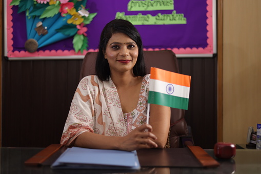 Proud school principal showcasing Indian  flag confidently sitting in her cabinet. looking into the camera.