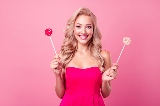 Portrait of nice funky lovely girl beaming smile hands hold sweet candy stick isolated on pink color background.