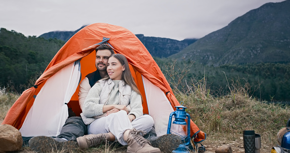 Camp, love and smile with a couple in a tent in the mountains together for travel, freedom or adventure in nature. Happy, romance or view with a man and woman outdoor for vacation in the wilderness