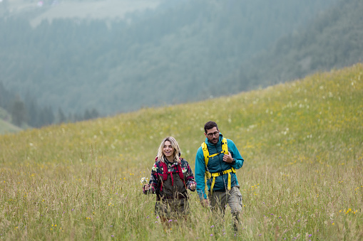 Happy couple of backpackers taking a walk through tall grass on a mountain. Copy space.