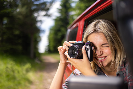 Happy woman having fun while taking a photo with digital camera during a trip by jeep.
