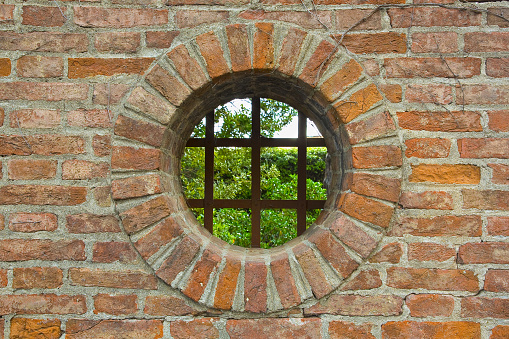 Round window on old and weathered brick wall with metal grate