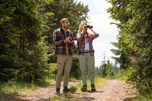 Young couple of tourist exploring the nature while woman is looking in the distance through binoculars.