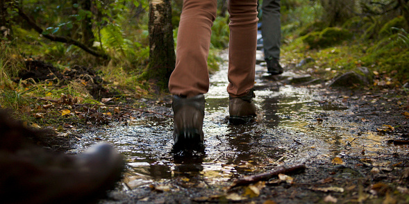 A video still of an unrecognisable group of people wearing hiking boots, walking through muddy puddles during a hike in Torridon, Scotland.