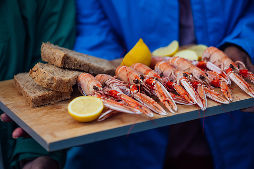 A close-up of freshly cooked langoustines, lemon and bread on a chopping board that an unrecognisable person is holding in Torridon, Scotland. They are ready to eat.