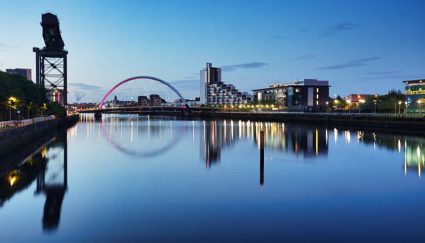 beautiful sunset clyde arc bridge across river in glasgow, scotland, uk. it is nice weather with reflection on water, blue sky, lights from buildings in downtown, skyline, attractions. - finnieston imagens e fotografias de stock