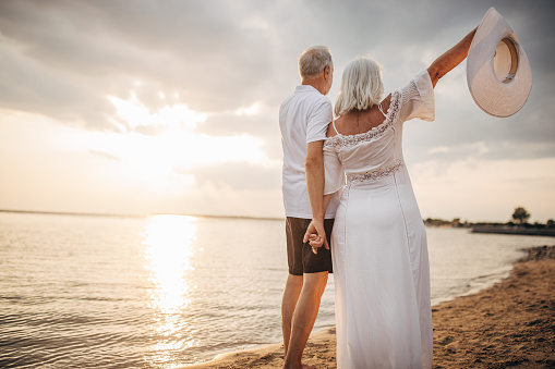Man and woman, happy senior couple standing on the beach by the sea together.
